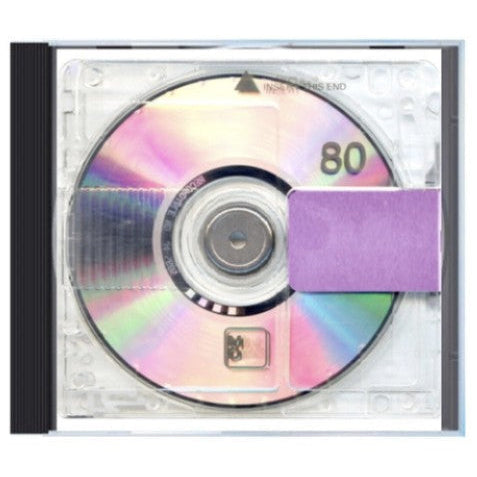 A CD jewel case containing a CD with an iridescent reflective surface, a purple rectangular sticker covering part of the disc, and a black spine on a white background.